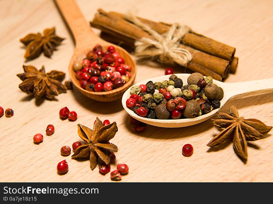 Wooden Spoons with a mixture of grains of pepper, cinnamon and star anise on a wooden surface