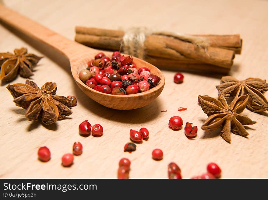 Wooden Spoon with a mixture of grains of pepper, cinnamon and star anise on a wooden surface