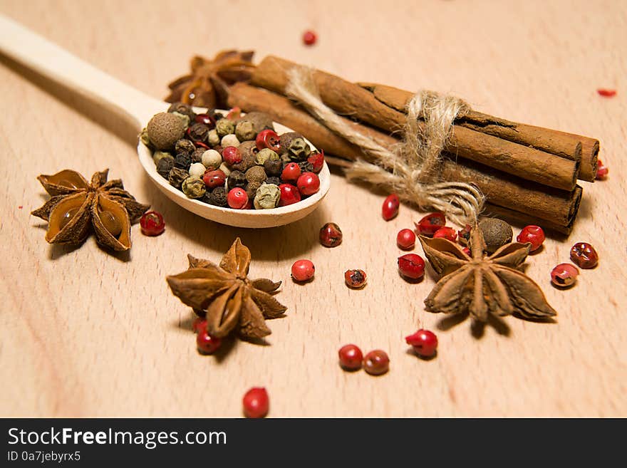 Wooden Spoon with a mixture of grains of pepper, cinnamon and star anise on a wooden surface