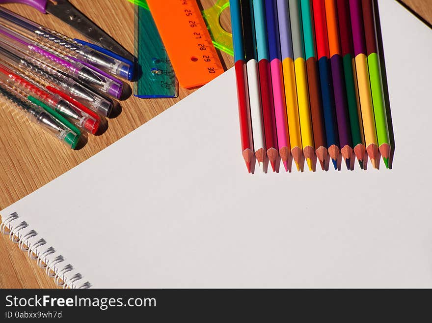 Colored pencils, pens, a ruler with a white notebook