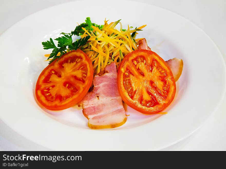 Fresh carrot salad with bacon and tomatoes on the plate closeup