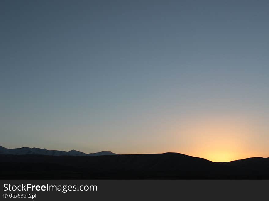 Mountain road in the remote northeastern Talas region of Kyrgyzstan, central Asia. Sun setting behind the mountains. Mountain road in the remote northeastern Talas region of Kyrgyzstan, central Asia. Sun setting behind the mountains.