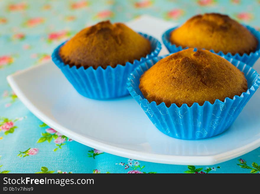 Muffins in the blue paper cupcake holder on a white plate, azure napkin floral print, selective focus. Muffins in the blue paper cupcake holder on a white plate, azure napkin floral print, selective focus