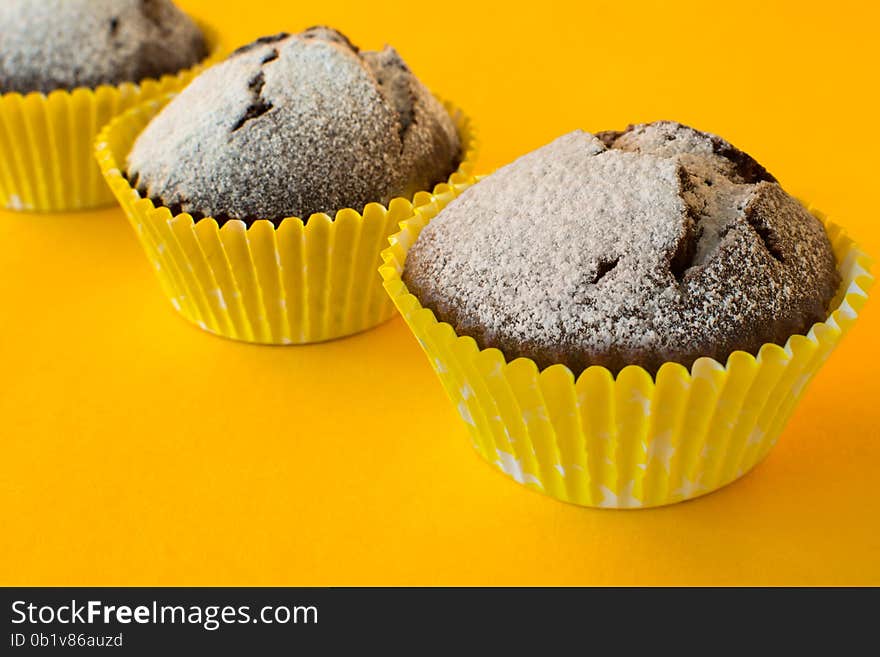 Chocolate muffins in paper cupcake holder on yellow background, selective focus. Chocolate muffins in paper cupcake holder on yellow background, selective focus