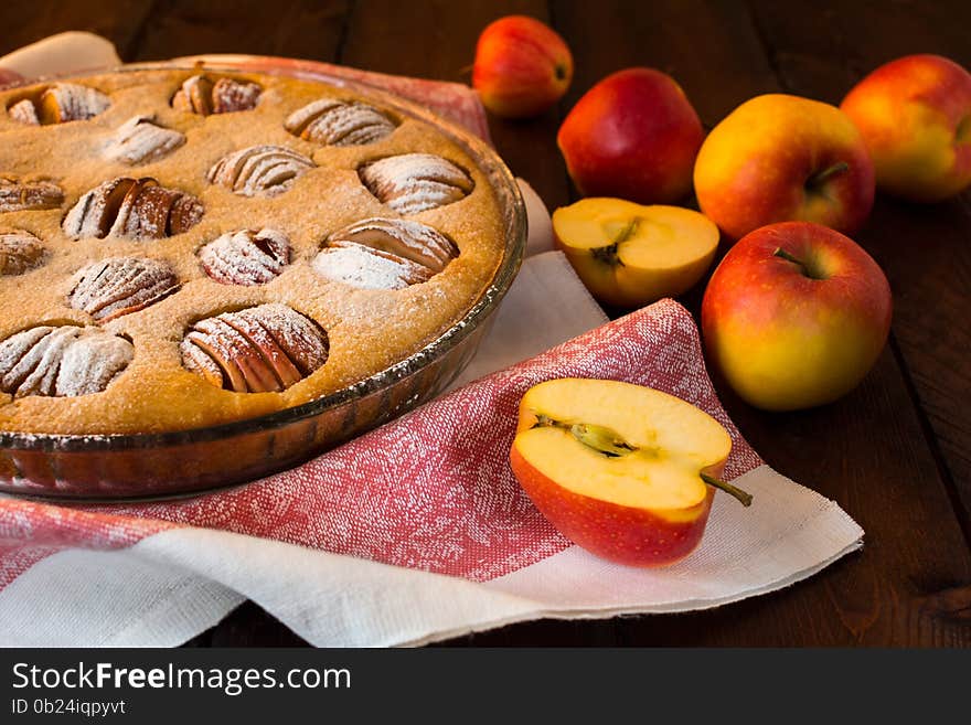 Apple pie in a baking dish, linen napkin and apples on dark background, selective focus. Apple pie in a baking dish, linen napkin and apples on dark background, selective focus