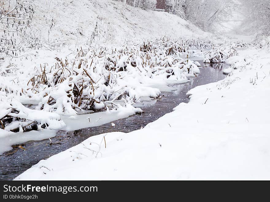 A small river cuts its way through snow covered landscape. It is still snowing and the river is freezing bit by bit. A small river cuts its way through snow covered landscape. It is still snowing and the river is freezing bit by bit.