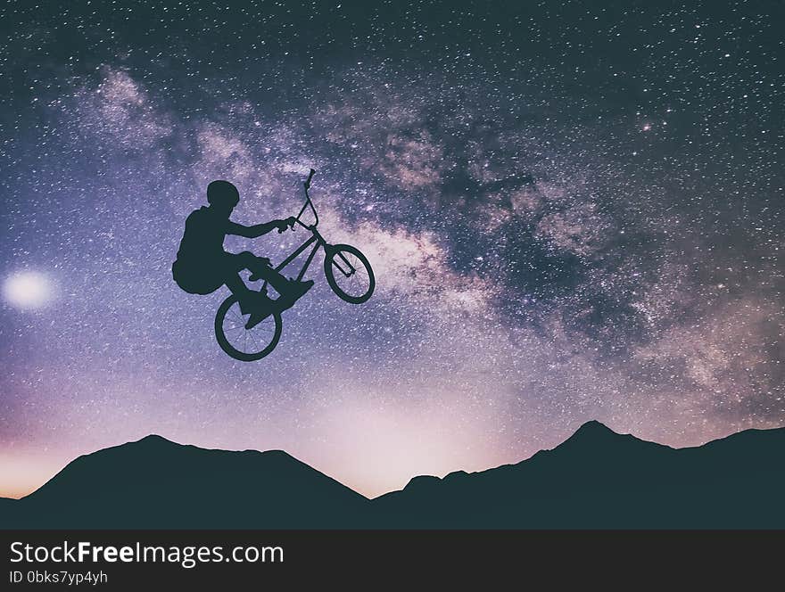 Man riding a bike performing a trick against on Mountain with Milky way. Man riding a bike performing a trick against on Mountain with Milky way.