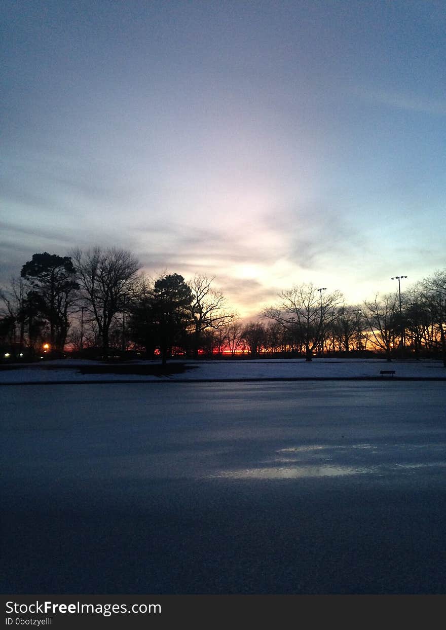 Sunset In A Park With Ice On Frozen Pond In Winter.