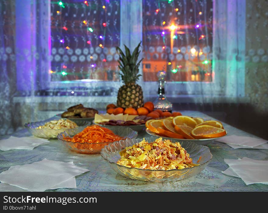 Festively laid table with salads, pineapple, meat, wine and tangerines at night. Festively laid table with salads, pineapple, meat, wine and tangerines at night