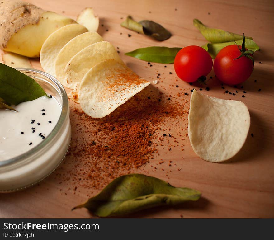 Potato chip manufacturing process. Potatoes, chips, tomatoes, sauce, spices, bay leaves, cumin, paprika on a wooden background. Potato chip manufacturing process. Potatoes, chips, tomatoes, sauce, spices, bay leaves, cumin, paprika on a wooden background.