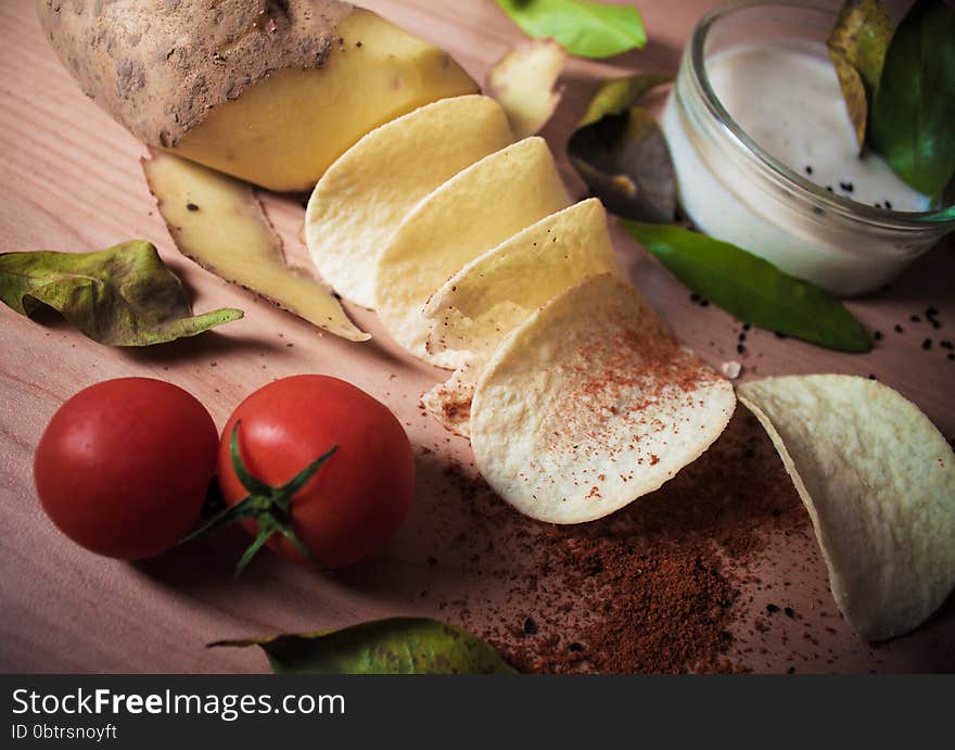 Potato chip manufacturing process. Potatoes, chips, tomatoes, sauce, spices, bay leaves, cumin, paprika on a wooden background. Potato chip manufacturing process. Potatoes, chips, tomatoes, sauce, spices, bay leaves, cumin, paprika on a wooden background.