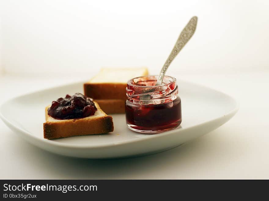 A mason jar of jam and bread on a white plate