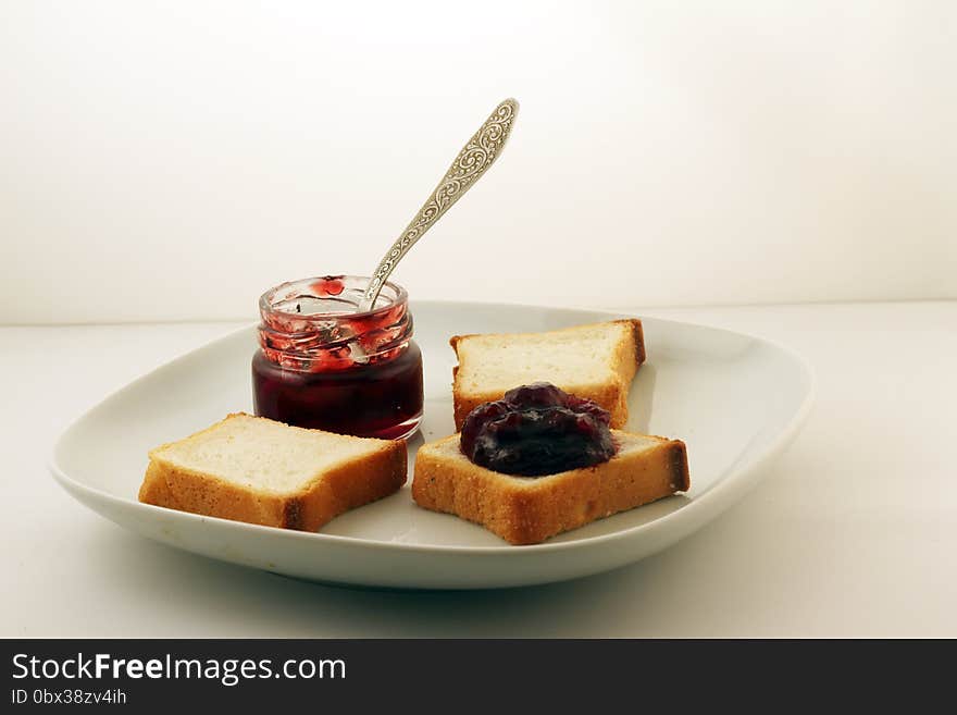 A mason jar of jam and bread on a white plate