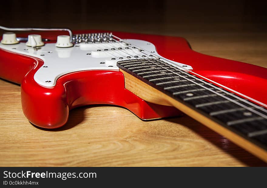 Body part of red 6 string electric guitar lying on the wooden floor closeup. Body part of red 6 string electric guitar lying on the wooden floor closeup