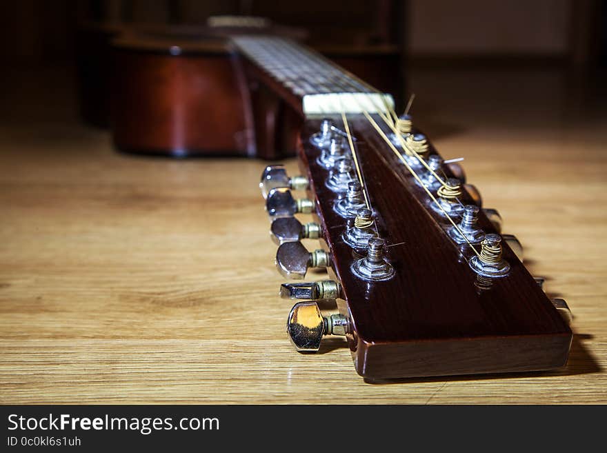 Brown head neck of 12 string guitar lyinh on wooden floor closeup. Brown head neck of 12 string guitar lyinh on wooden floor closeup