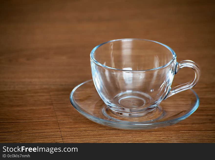 Glass cup and saucer on wooden table closeup