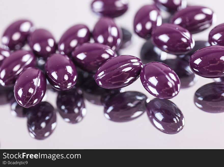 Capsules purple pills on the mirror surface close up, macro, photos with depth of field. Capsules purple pills on the mirror surface close up, macro, photos with depth of field