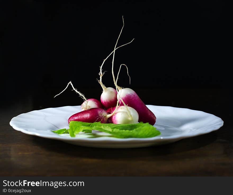 Fresh radishes in white plate on old wooden table