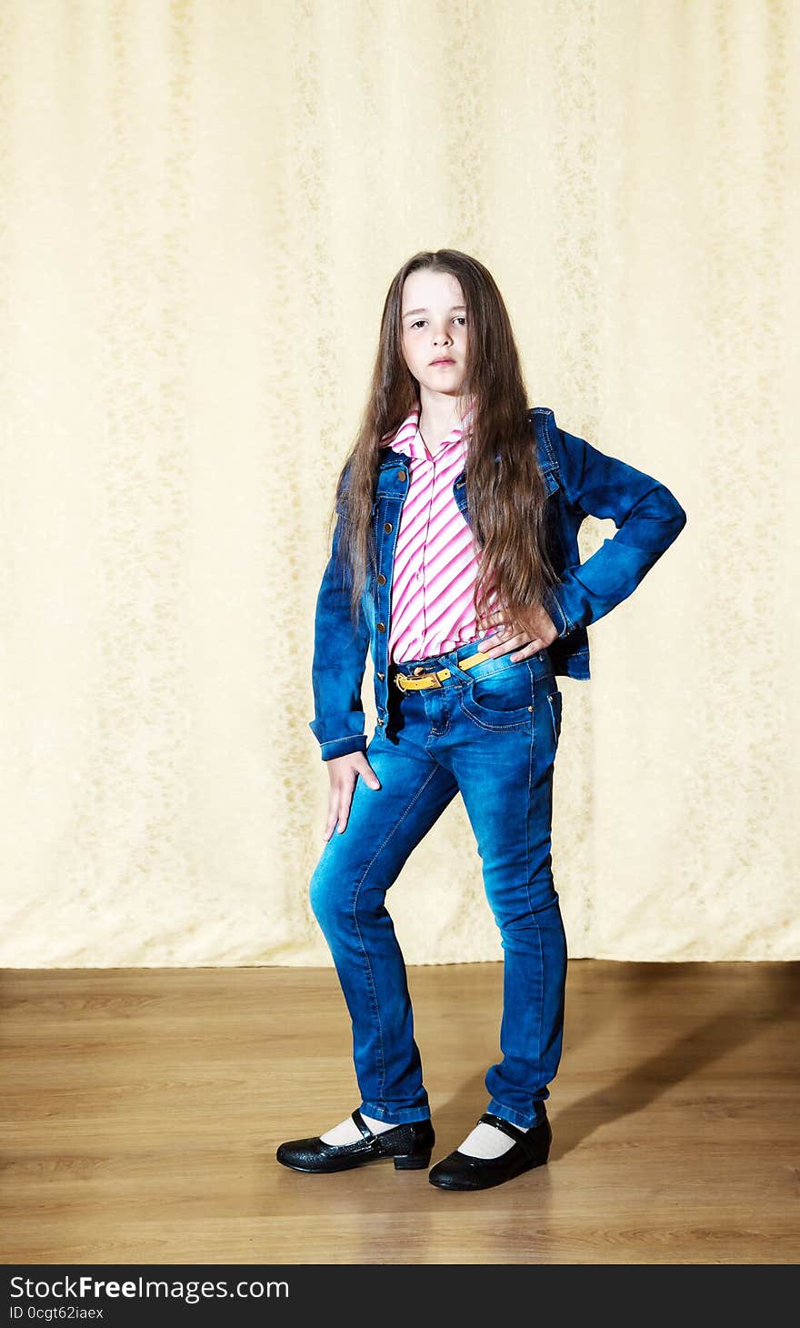 Little girl with long hair in a blue denim suit posing while standing in the studio