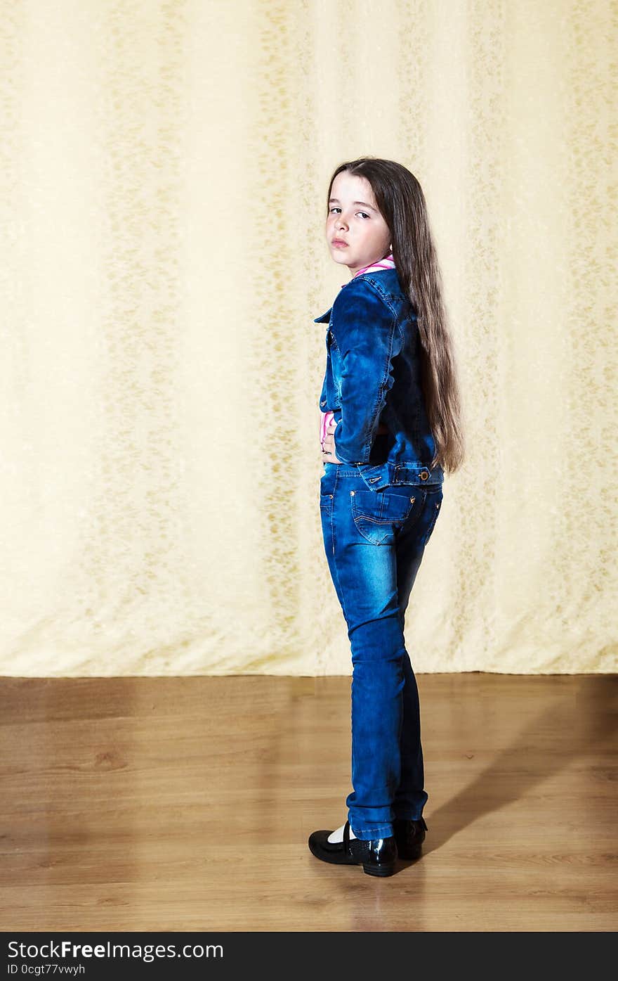 Little girl with long hair in a blue denim suit posing while standing in the studio