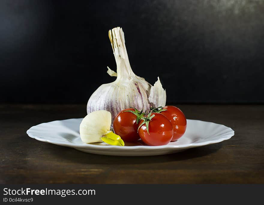 Tomatoes and clove of garlic in white plate. Tomatoes and clove of garlic in white plate