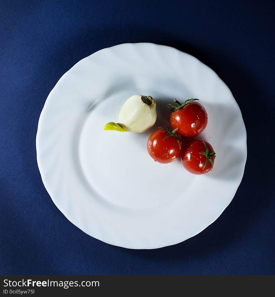 Tomatoes and clove of garlic in white plate on a dark blue background. Tomatoes and clove of garlic in white plate on a dark blue background