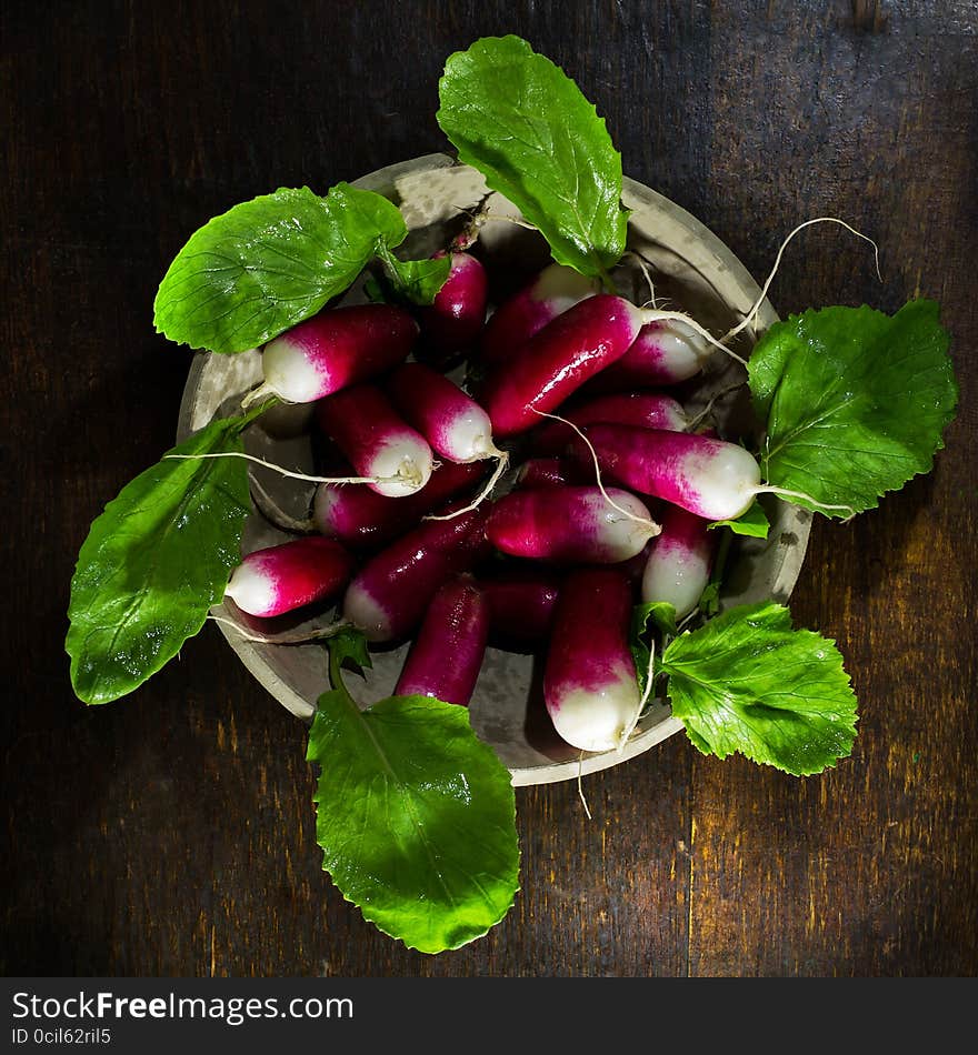 Fresh radishes in plate on old wooden table