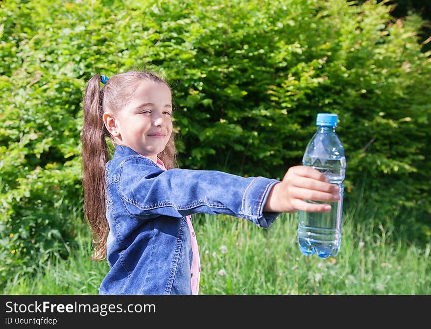 Girl in a blue denim jacket giving a plastic bottle with water. Girl in a blue denim jacket giving a plastic bottle with water