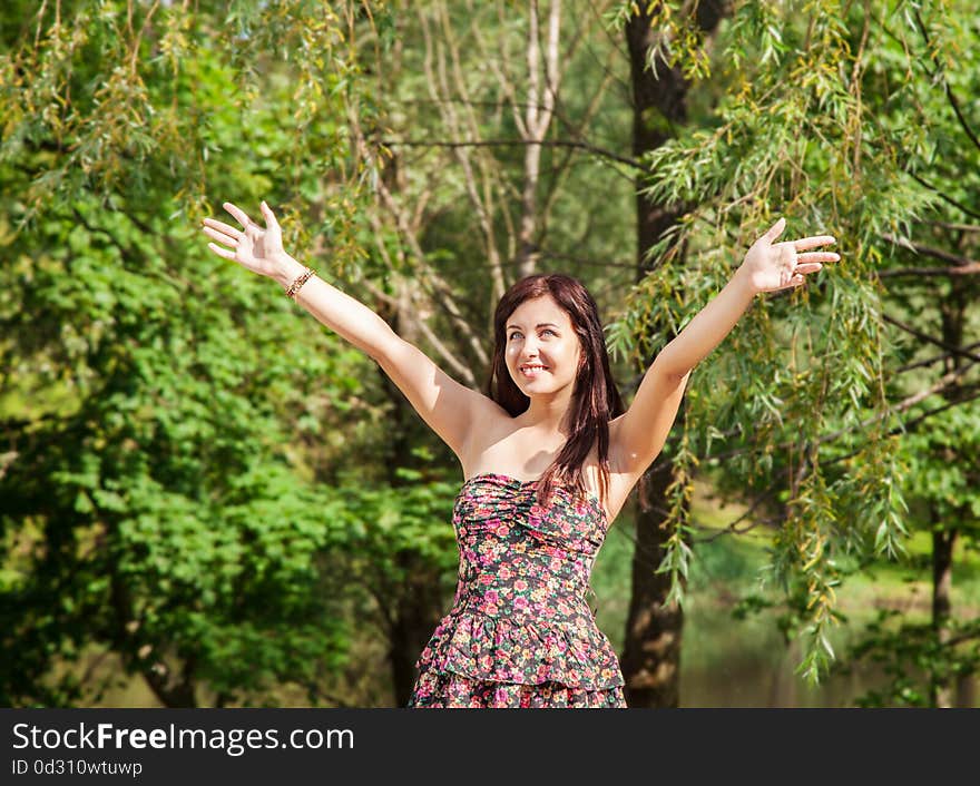 Young beautiful smiling girl holds out her hands to the sky in the park on summer day