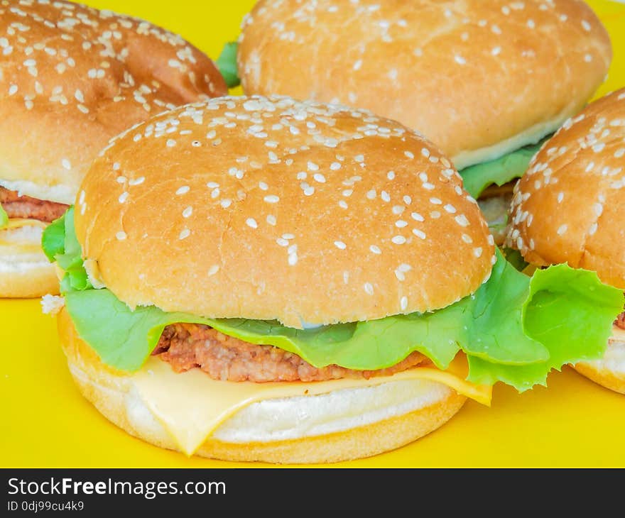 Picture with delicious beef hamburger with salad and cheese on a yellow plate. Picture with delicious beef hamburger with salad and cheese on a yellow plate