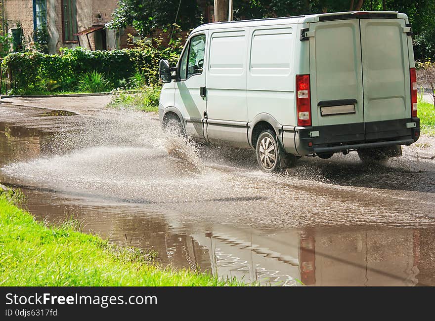 White commercial vehicle riding on big puddle on the road in residental area on summer day. White commercial vehicle riding on big puddle on the road in residental area on summer day