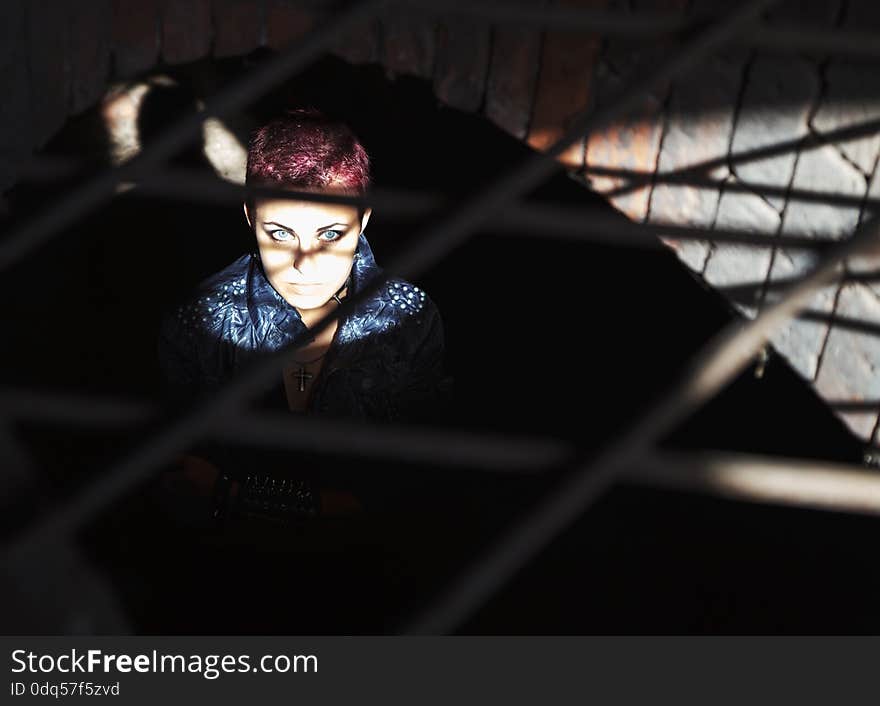 Punk girl sitting on the floor behind metal bars