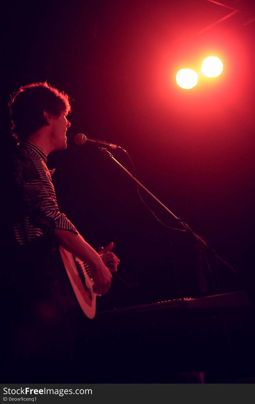 Singer playing acoustic guitar while performing onstage in spotlight. Singer playing acoustic guitar while performing onstage in spotlight.