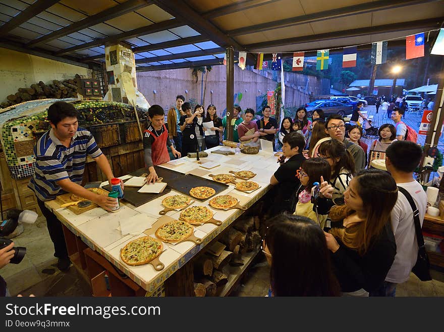 Patrons sitting at table inside pizzeria with workers assembling pies. Patrons sitting at table inside pizzeria with workers assembling pies.