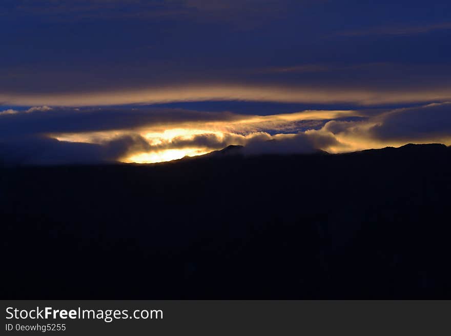 Sun setting through clouds in blue skies over landscape. Sun setting through clouds in blue skies over landscape.