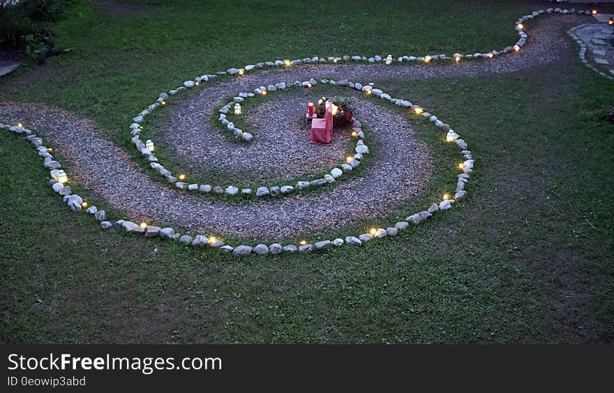 A garden path in the shape of a spiral with lanterns on the sides and a chair in the middle. A garden path in the shape of a spiral with lanterns on the sides and a chair in the middle.