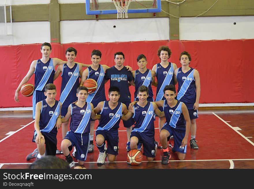 Basketball team posing in uniform as group with coach inside gymnasium court.