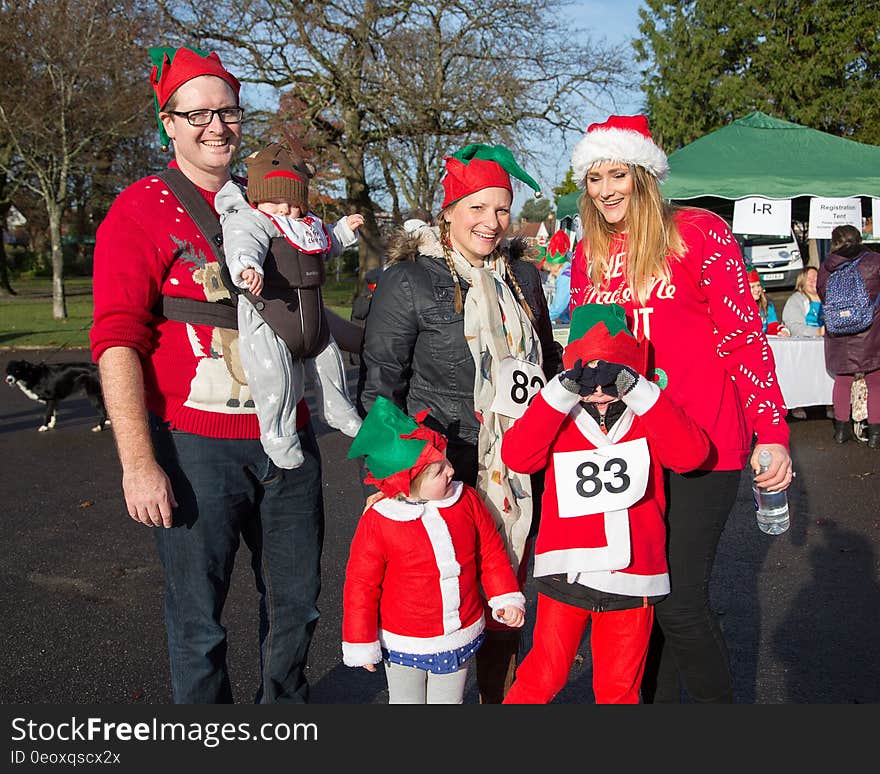 People in elf costumes and Santa hats standing outdoors in Christmas parade or walk.