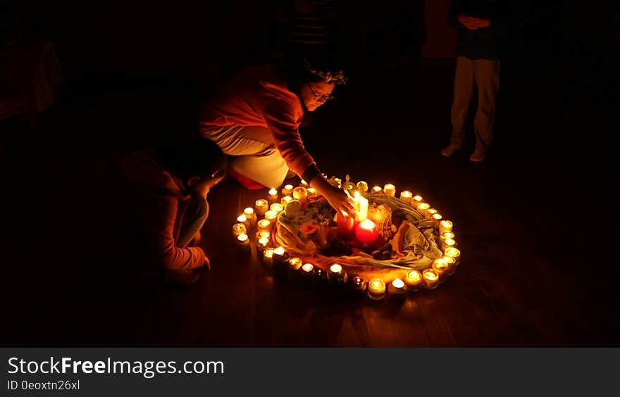 A circle of burning candles and a few people around it, a woman putting one in the middle.