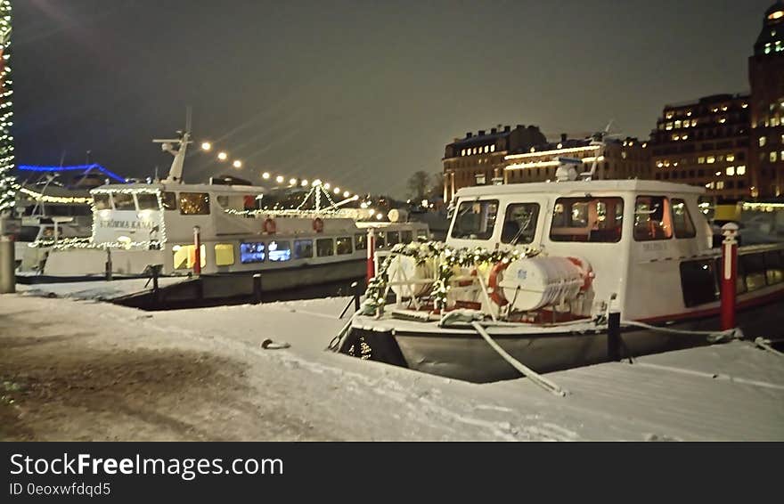 Boats moored to docks in snow covered harbor in city at night. Boats moored to docks in snow covered harbor in city at night.