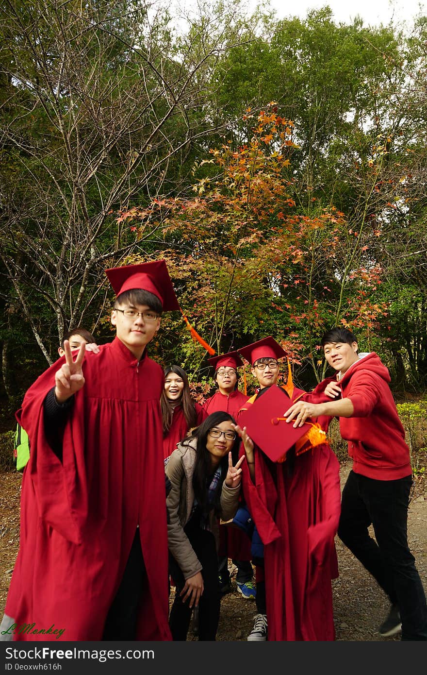 Graduating boys and girls in red mortar board caps and gowns in outdoor group portrait. Graduating boys and girls in red mortar board caps and gowns in outdoor group portrait.