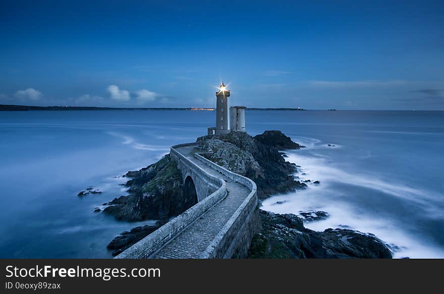 Exterior of lighthouse at end of winding path along rocky coastline illuminated at twilight. Exterior of lighthouse at end of winding path along rocky coastline illuminated at twilight.