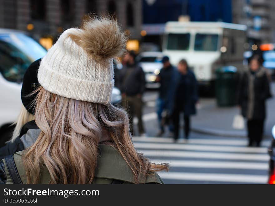 Woman in a white knitted tea cozy hat chatting to another person beside a designated crossing on a major road through the town. Woman in a white knitted tea cozy hat chatting to another person beside a designated crossing on a major road through the town.