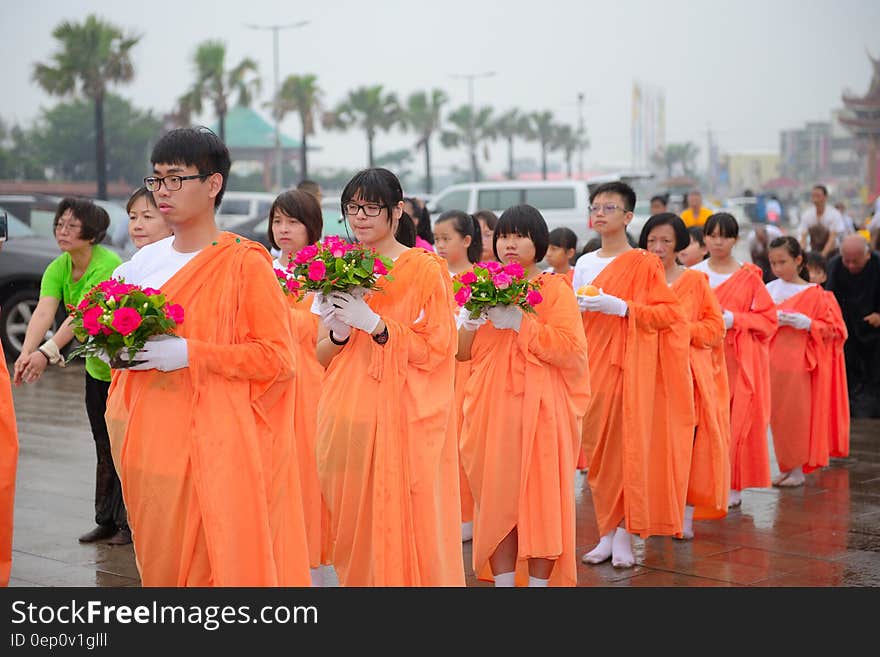 Children in orange robes holding flowers in outdoor religious procession.