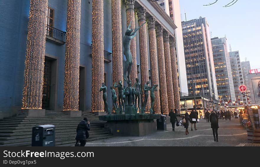 Pillars and statue outside modern urban architecture with crowds on sidewalk at twilight. Pillars and statue outside modern urban architecture with crowds on sidewalk at twilight.