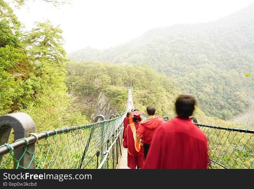 Graduates in cap and gown walking across suspension bridge in countryside on sunny day. Graduates in cap and gown walking across suspension bridge in countryside on sunny day.