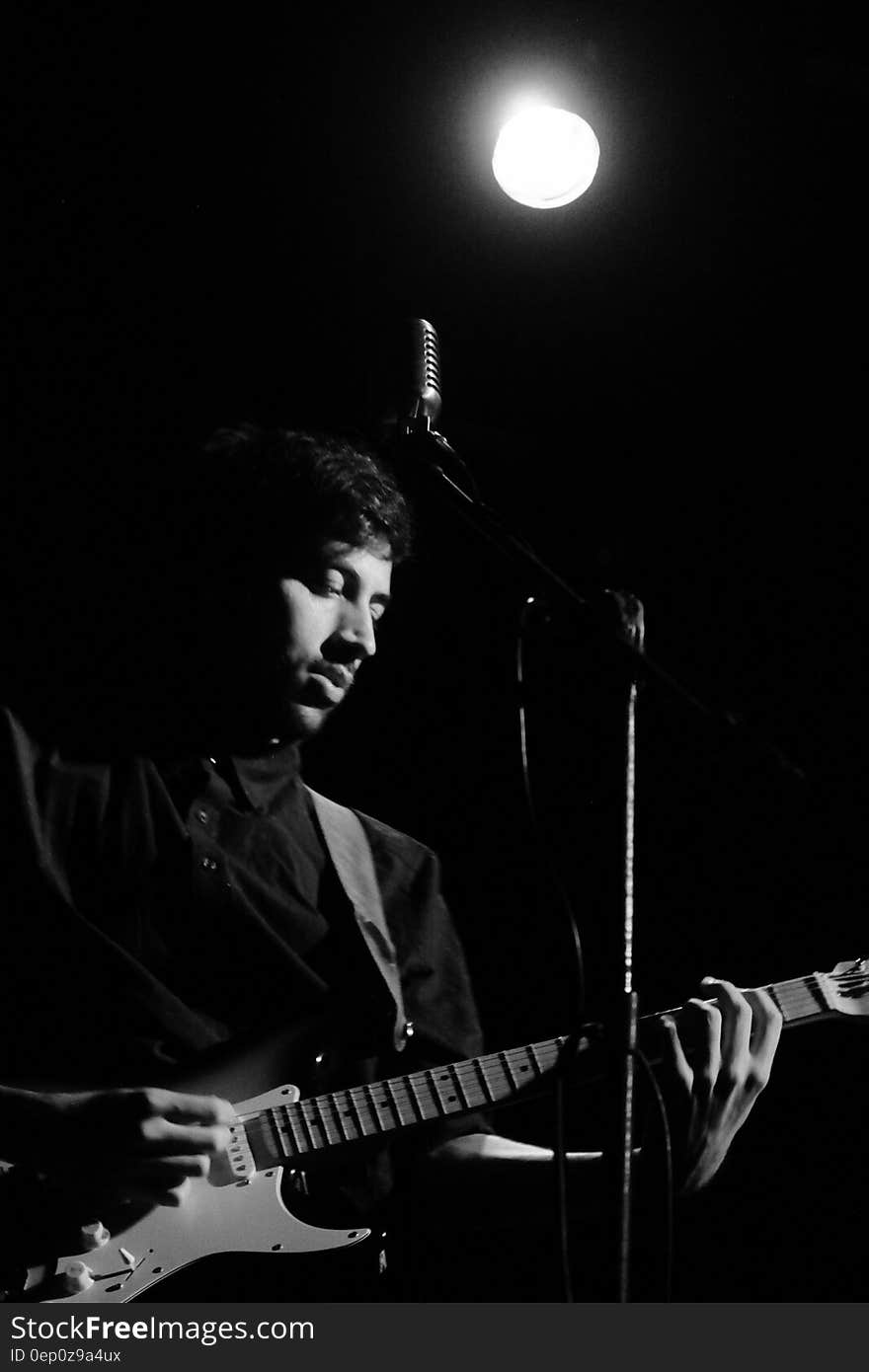 Musician playing guitar in front of microphone onstage in black and white with spotlight. Musician playing guitar in front of microphone onstage in black and white with spotlight.