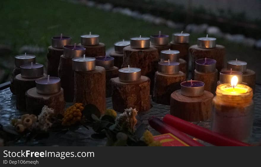 One lit and many unlit candles on outdoor display in evening.