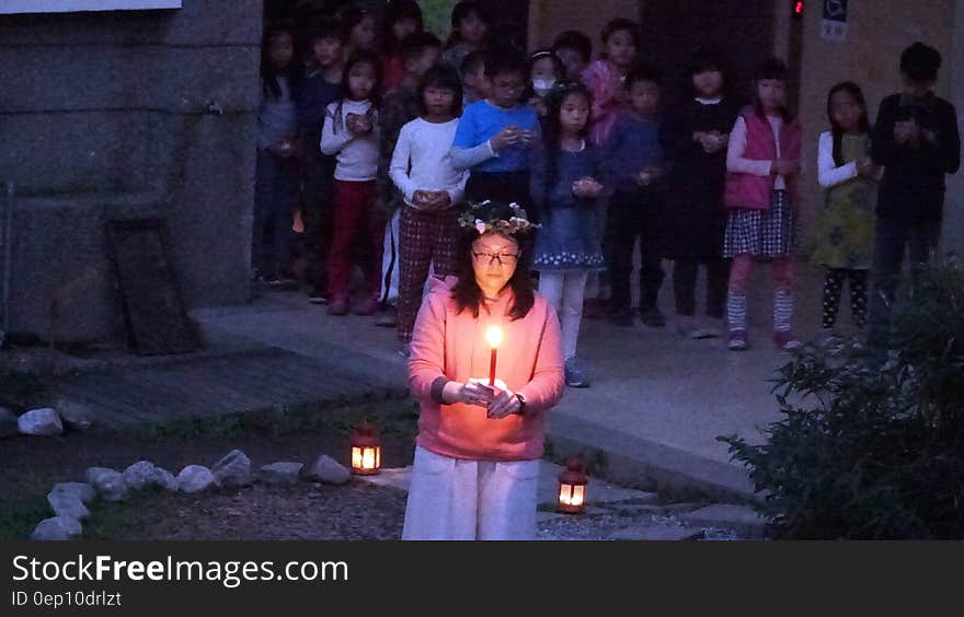 Girl carrying lit candle outdoors in garden illuminated with lamps. Girl carrying lit candle outdoors in garden illuminated with lamps.