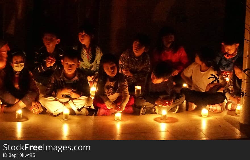 Children sitting on floor indoors illuminated by candlelight. Children sitting on floor indoors illuminated by candlelight.